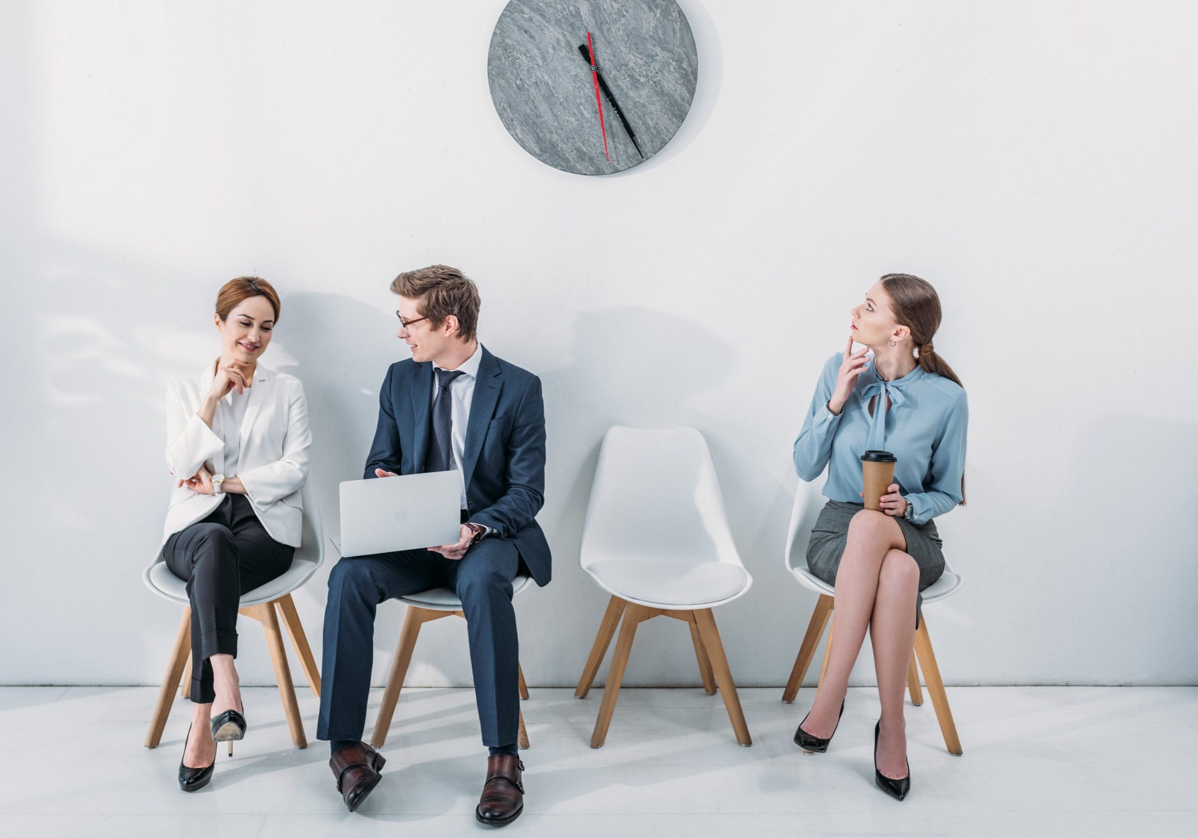 woman with paper cup looking at clock near employees sitting on chairs